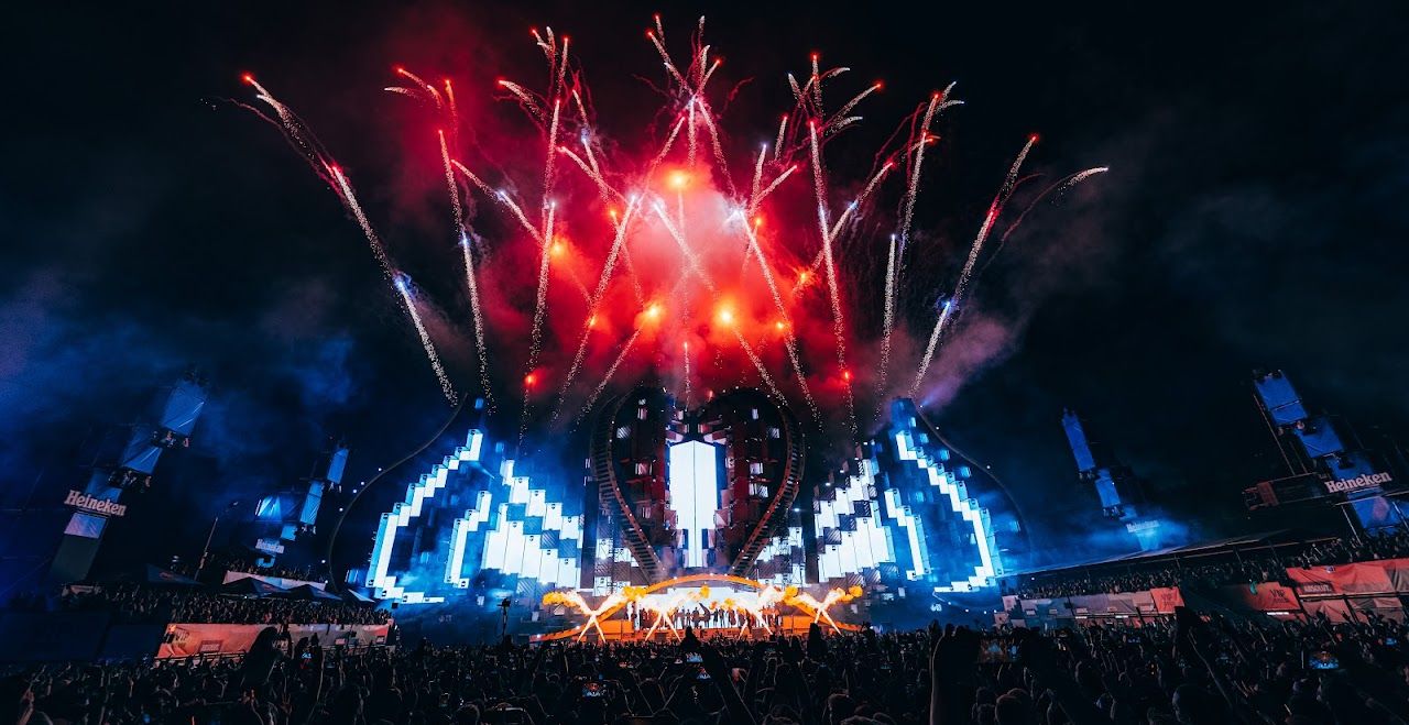 Large outdoor festival stage with fireworks and a crowd at night.