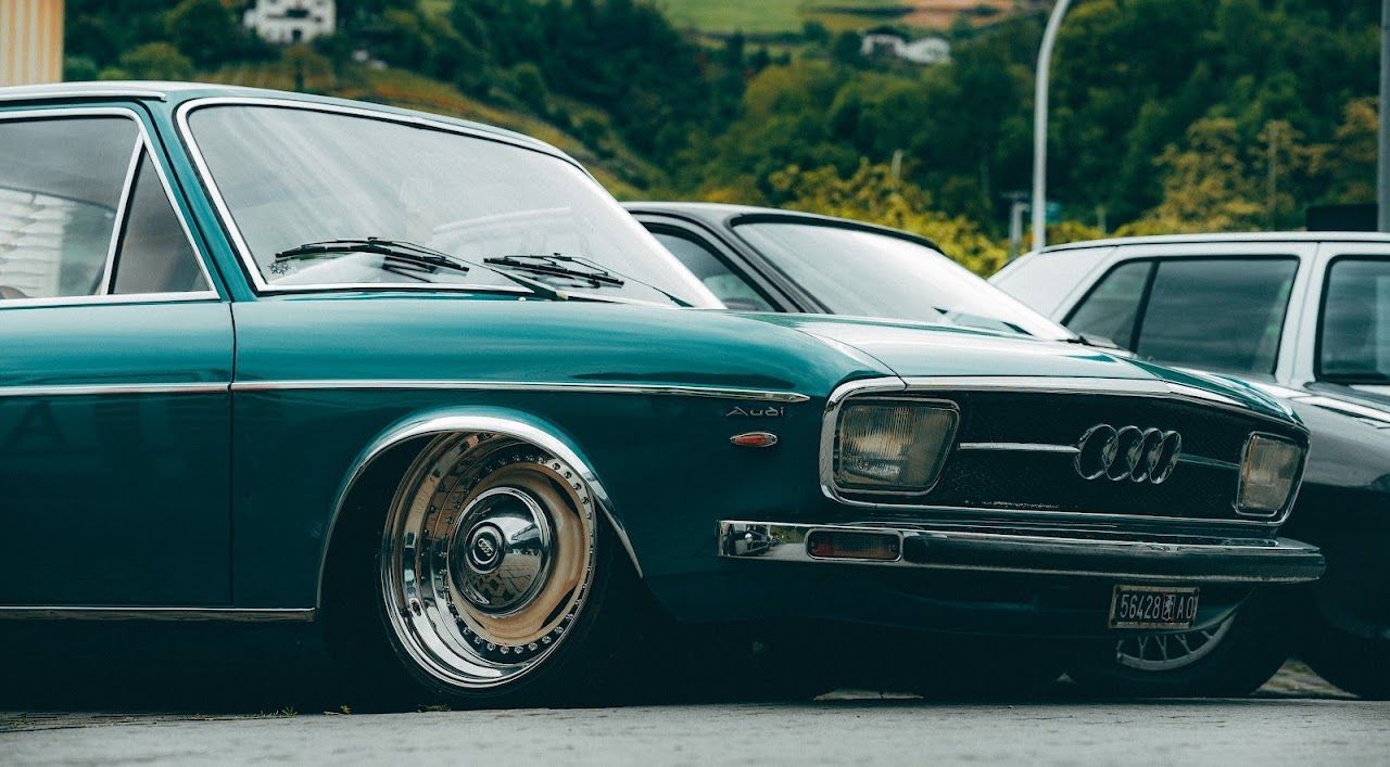 Classic green Audi car parked outdoors with other vehicles in the background.