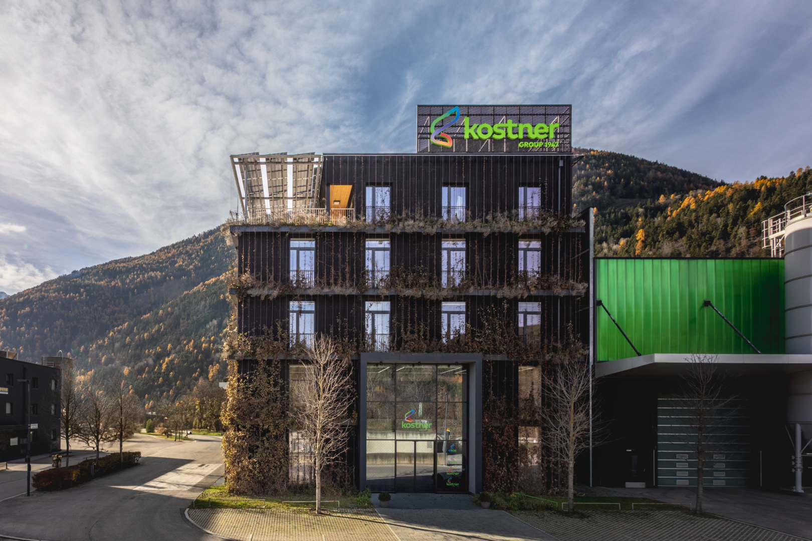 Modern office building with Kostner Group signage, surrounded by mountains and autumn trees.