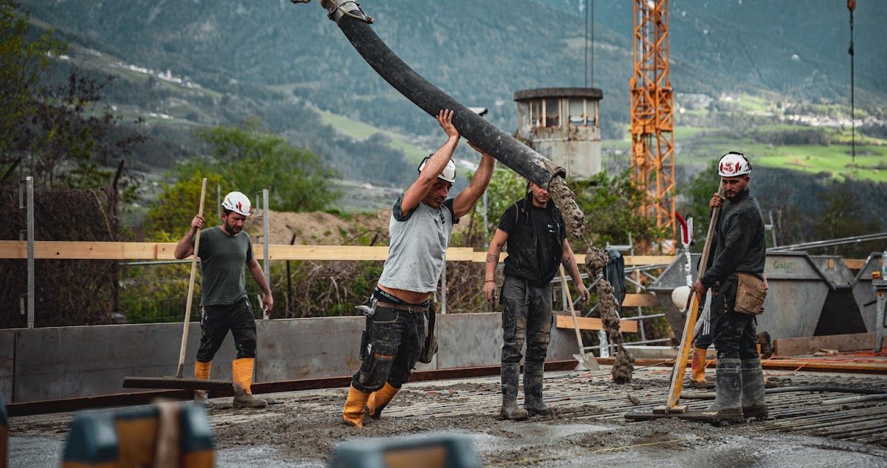 Construction workers pouring concrete on a building site with mountains in the background.