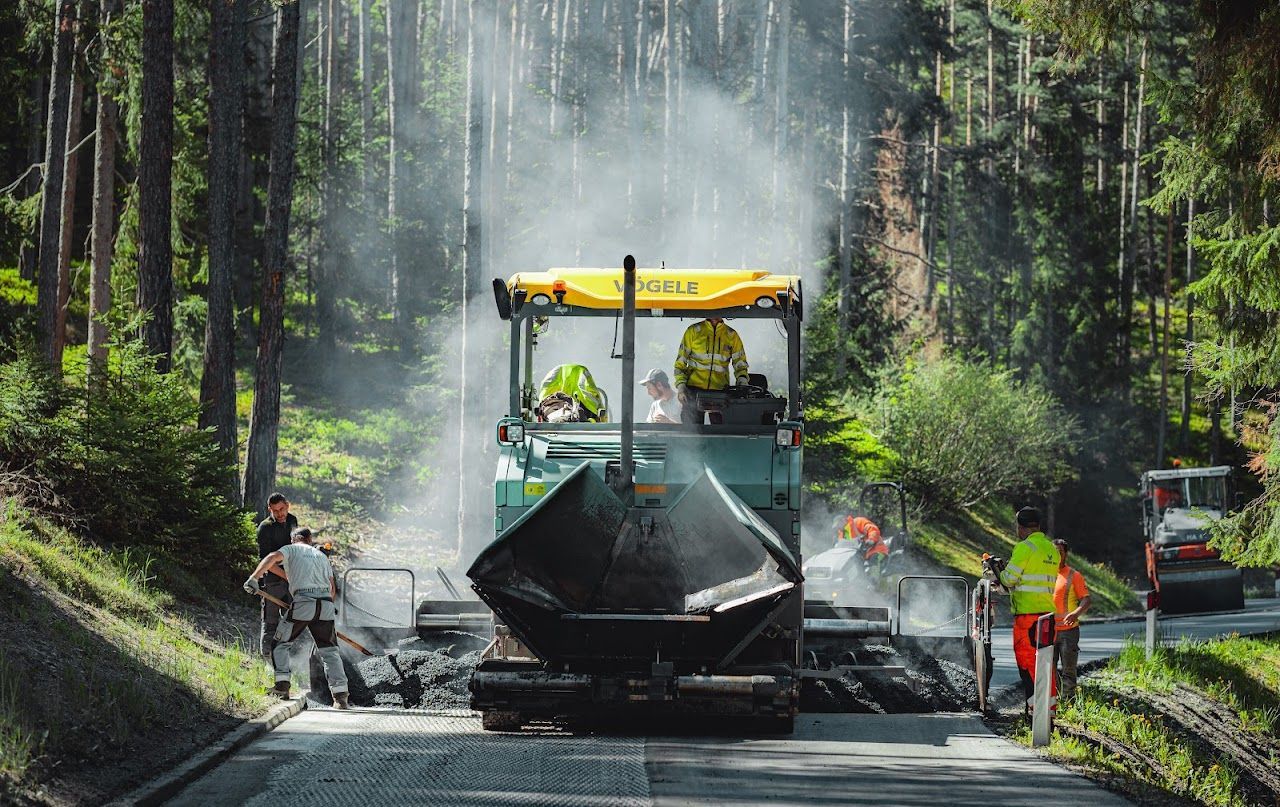 Road construction crew working with heavy machinery in a forested area.